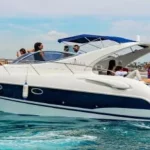 Yate pequeño con bandera de España y un grupo de chicos a bordo sobre agua cristalina